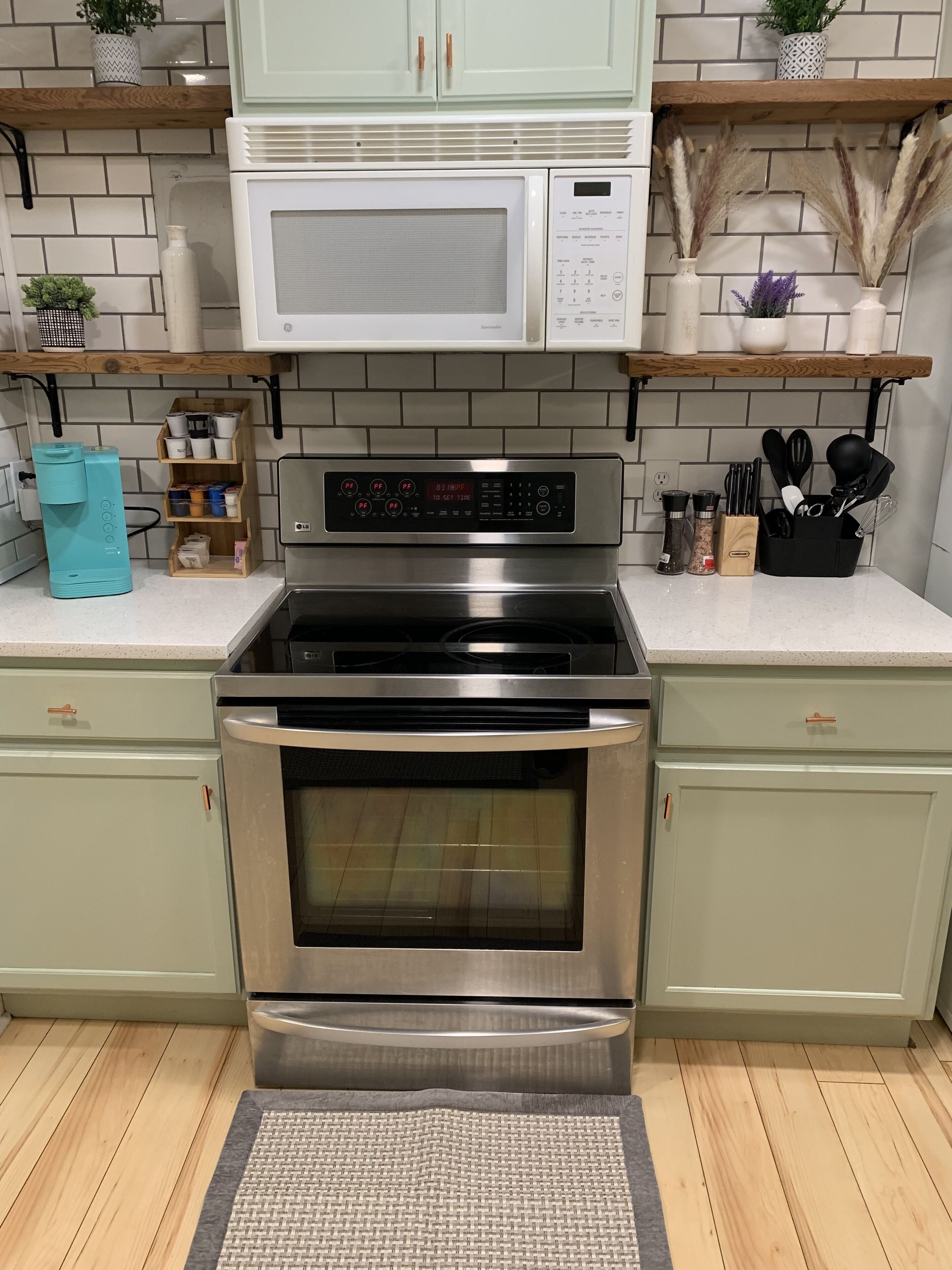 A kitchen with a stainless steel oven, a microwave, and a built-in range hood. There are wooden cabinets, a spice rack, and a coffee machine.