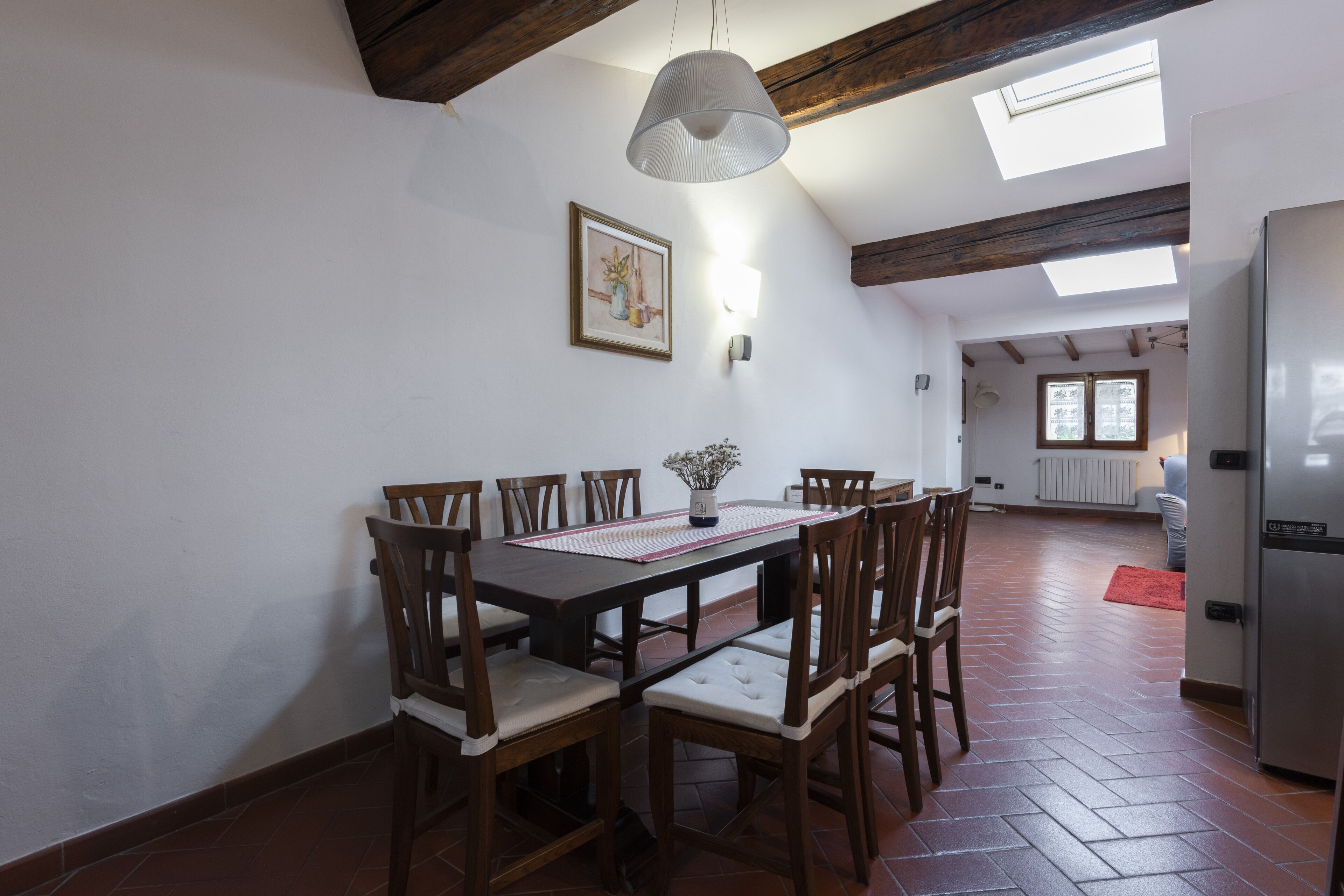 Zona pranzo con tavolo e sedie in legno, lampadario a sospensione e un lucernario.