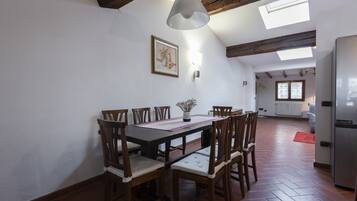 Zona pranzo con tavolo e sedie in legno, lampadario a sospensione e un lucernario.