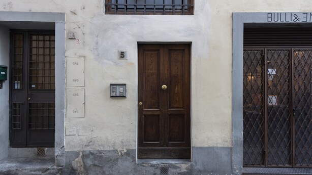 A building facade with a central wooden door, a window with metal bars, and a sign above the door. - Toscanella 3 Bedrooms by Mmega (Florence)