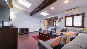 A spacious living room with a large grey sofa, a wooden coffee table, and a red rug. There is a television on a wooden cabinet, and an air conditioning unit mounted on the wall. - Toscanella 3 Bedrooms by Mmega (Florence)