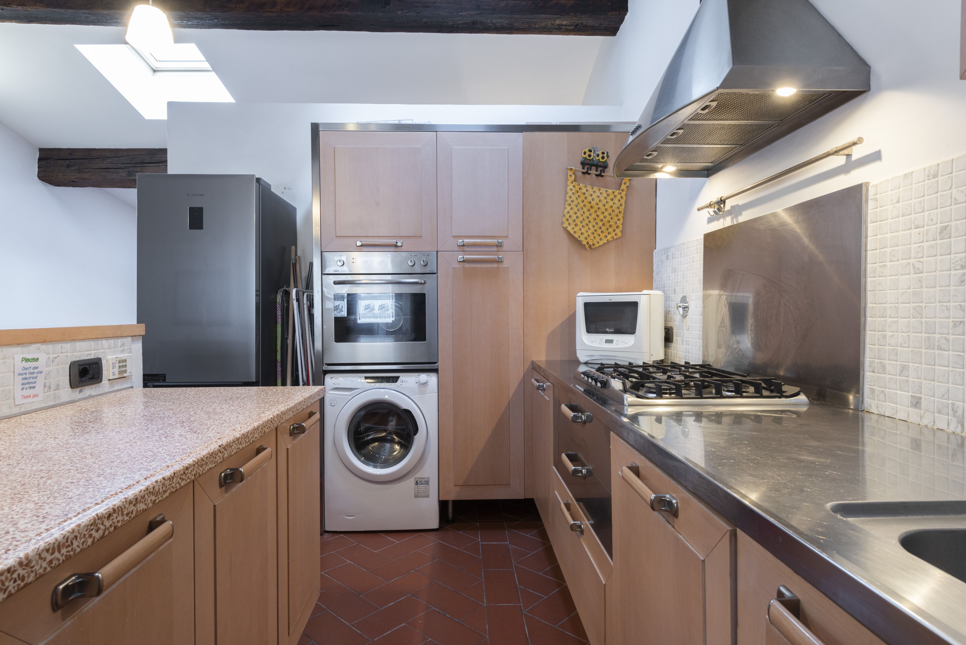 A compact kitchen with a stainless steel refrigerator, oven, microwave, and washing machine.