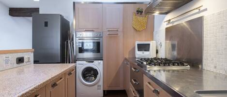 A compact kitchen with a stainless steel refrigerator, oven, microwave, and washing machine.