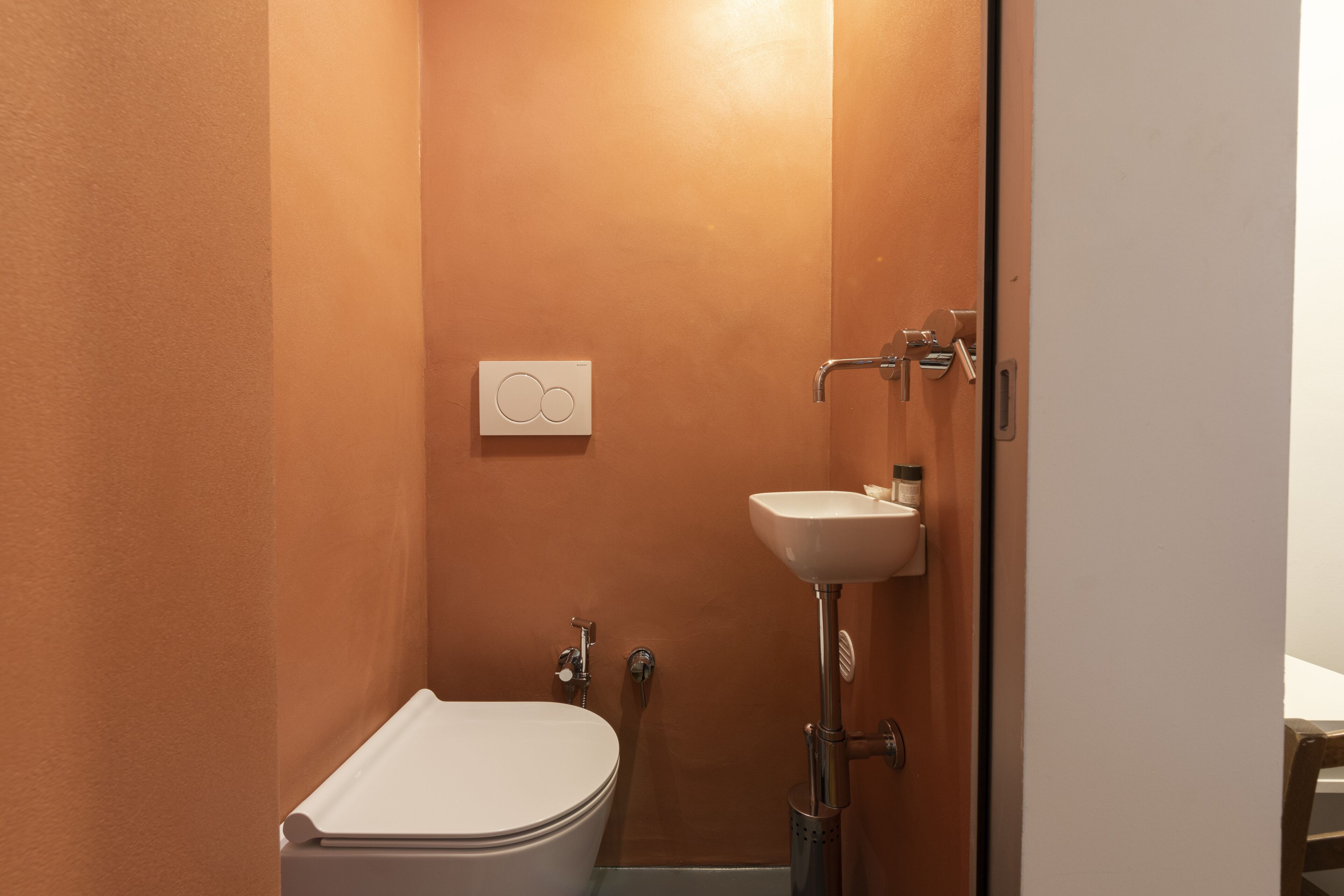 A small bathroom with a toilet, sink, and a wall-mounted control panel.