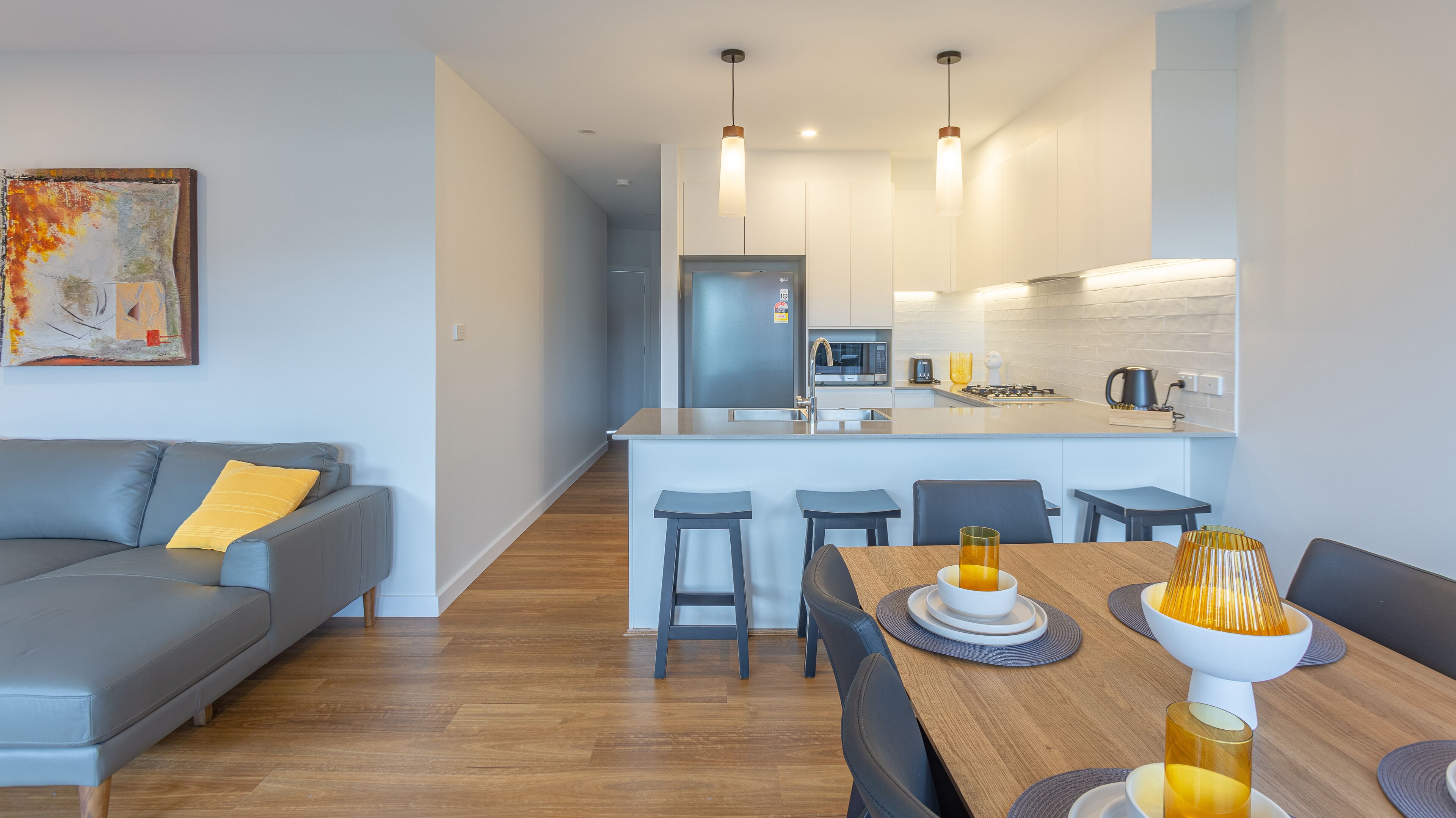 Een modern appartement met een grijze bank, een eettafel met stoelen, een keuken met een centraal kookeiland en een klein keukentje.