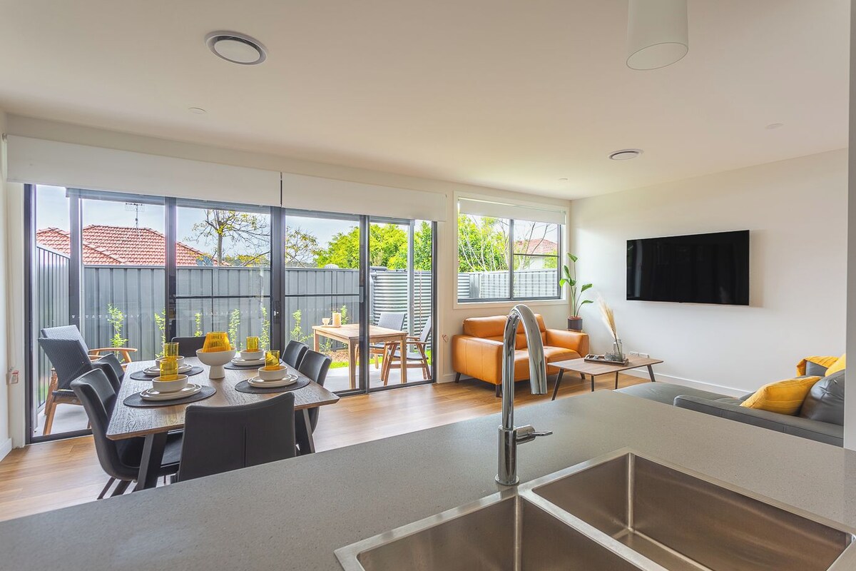 A modern kitchen with a dining area, large sliding glass doors to a backyard, and a flat-screen TV mounted on the wall.