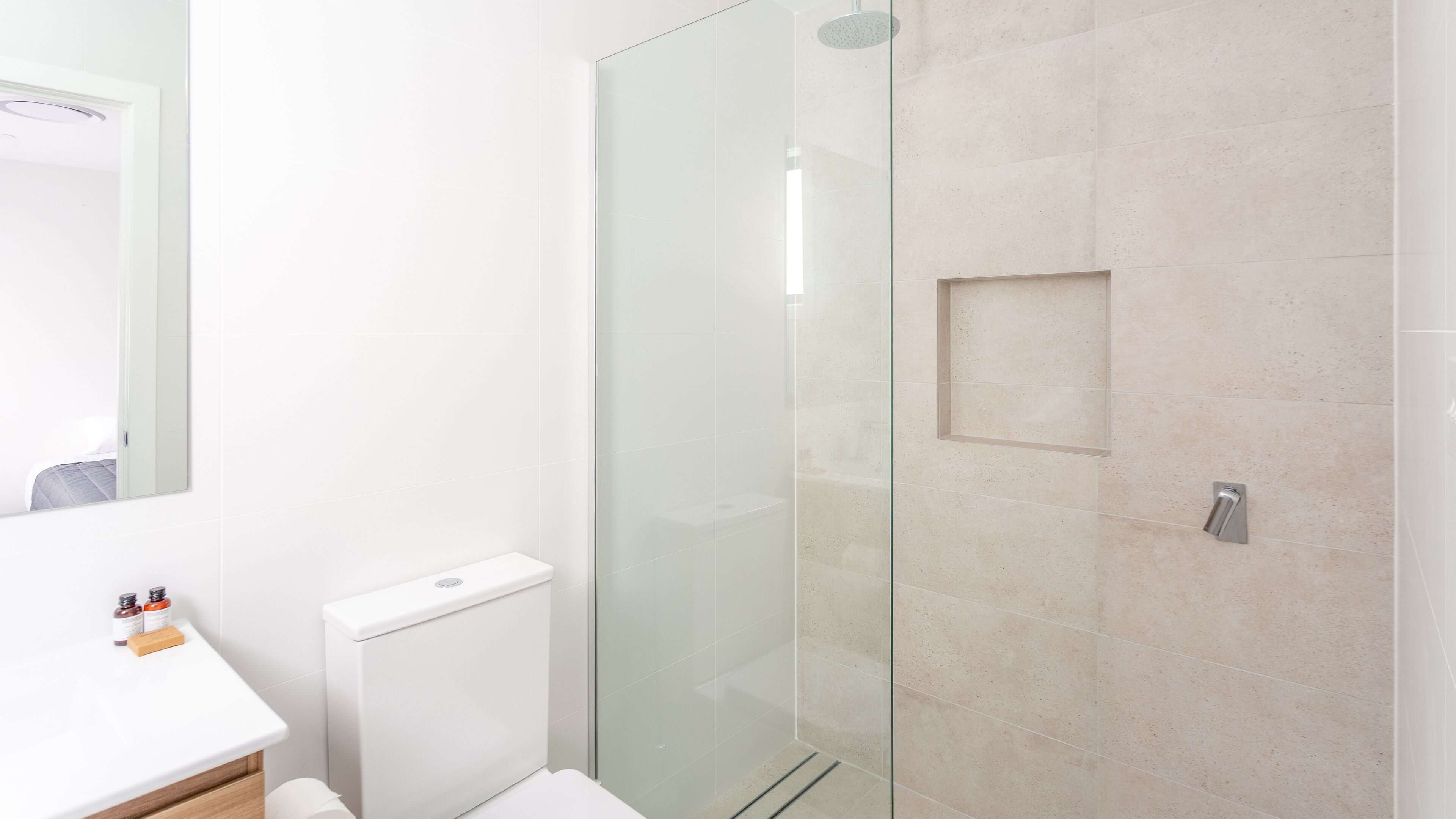 A modern bathroom with a glass shower enclosure, a toilet, and a sink with toiletries.