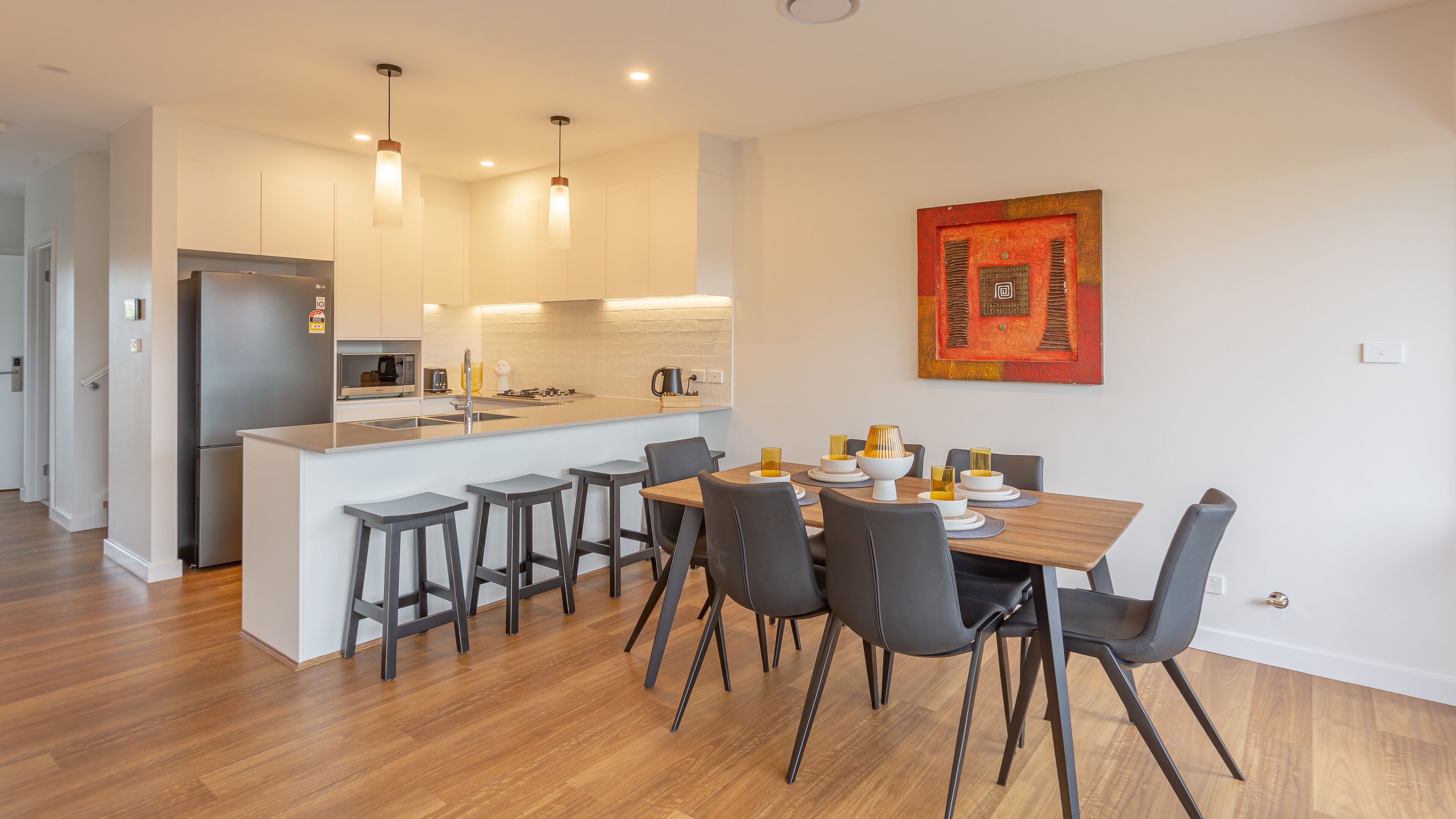 A modern kitchen with a central island, bar stools, and a dining table with chairs.