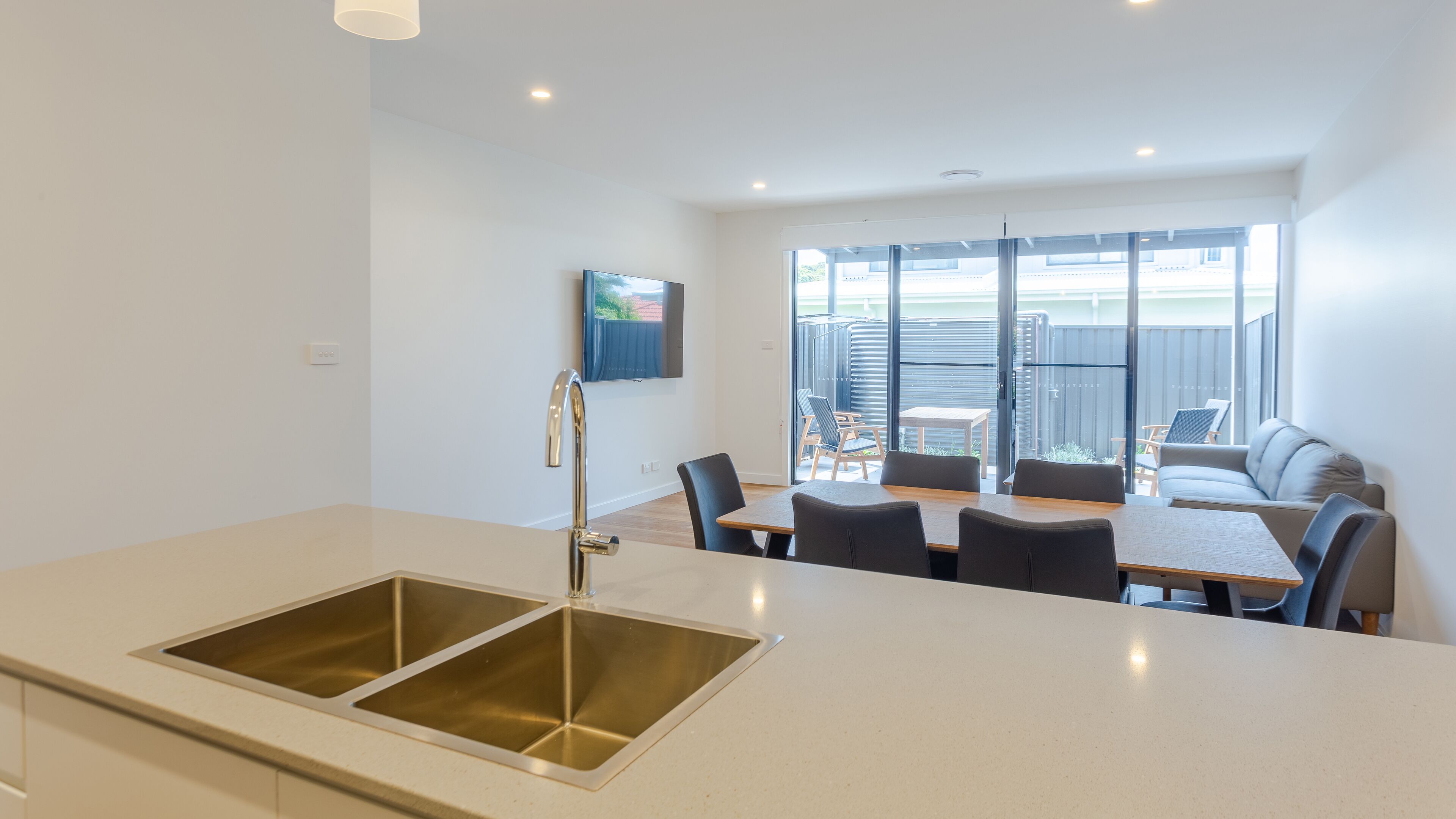 A modern kitchen with a stainless steel sink, a dining area with a table and chairs, and a view of the outside balcony.