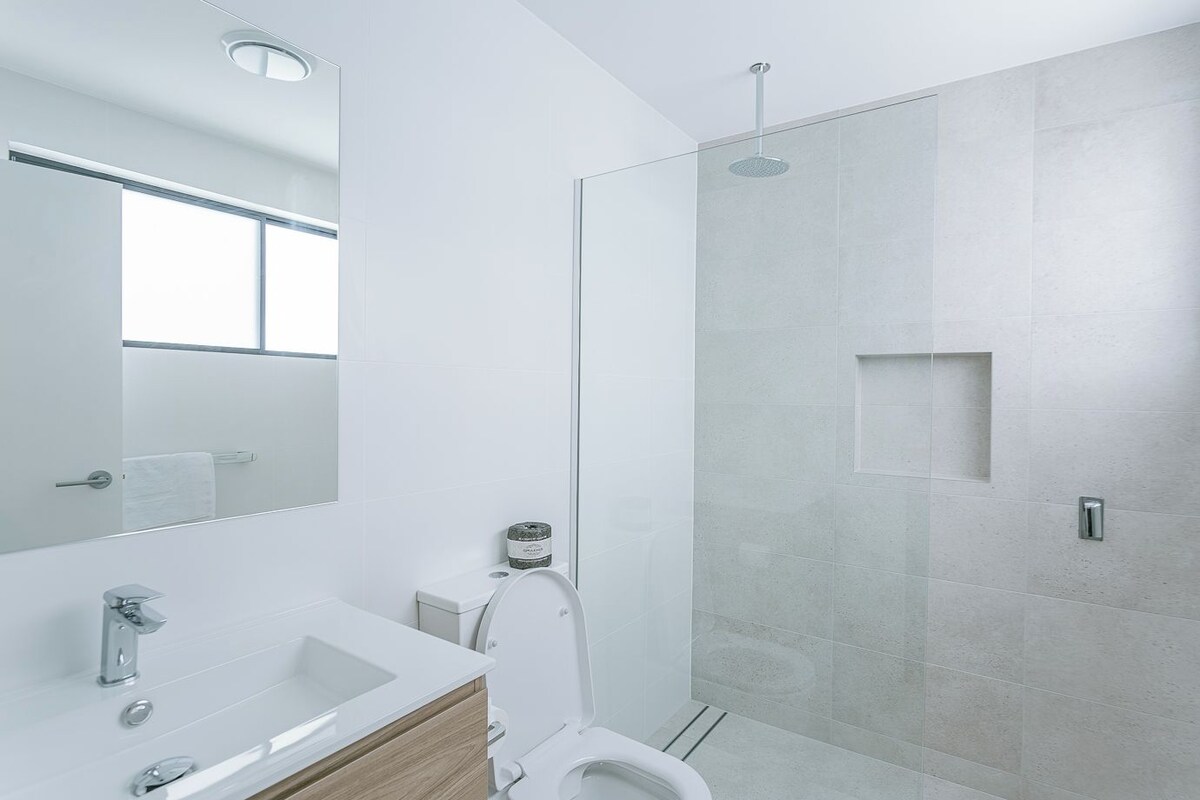 A modern bathroom with a glass shower enclosure, a white sink, and a mirror.