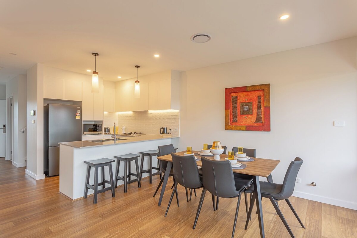 A modern kitchen with a central island, bar stools, and a dining table with chairs.
