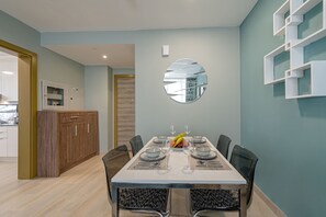 A dining area with a rectangular table set for six, surrounded by chairs. A wooden cabinet and a mirror are visible in the background. - Marco Polo - Park and Skyline Views From this Cozy Apt in JVC (Dubai)