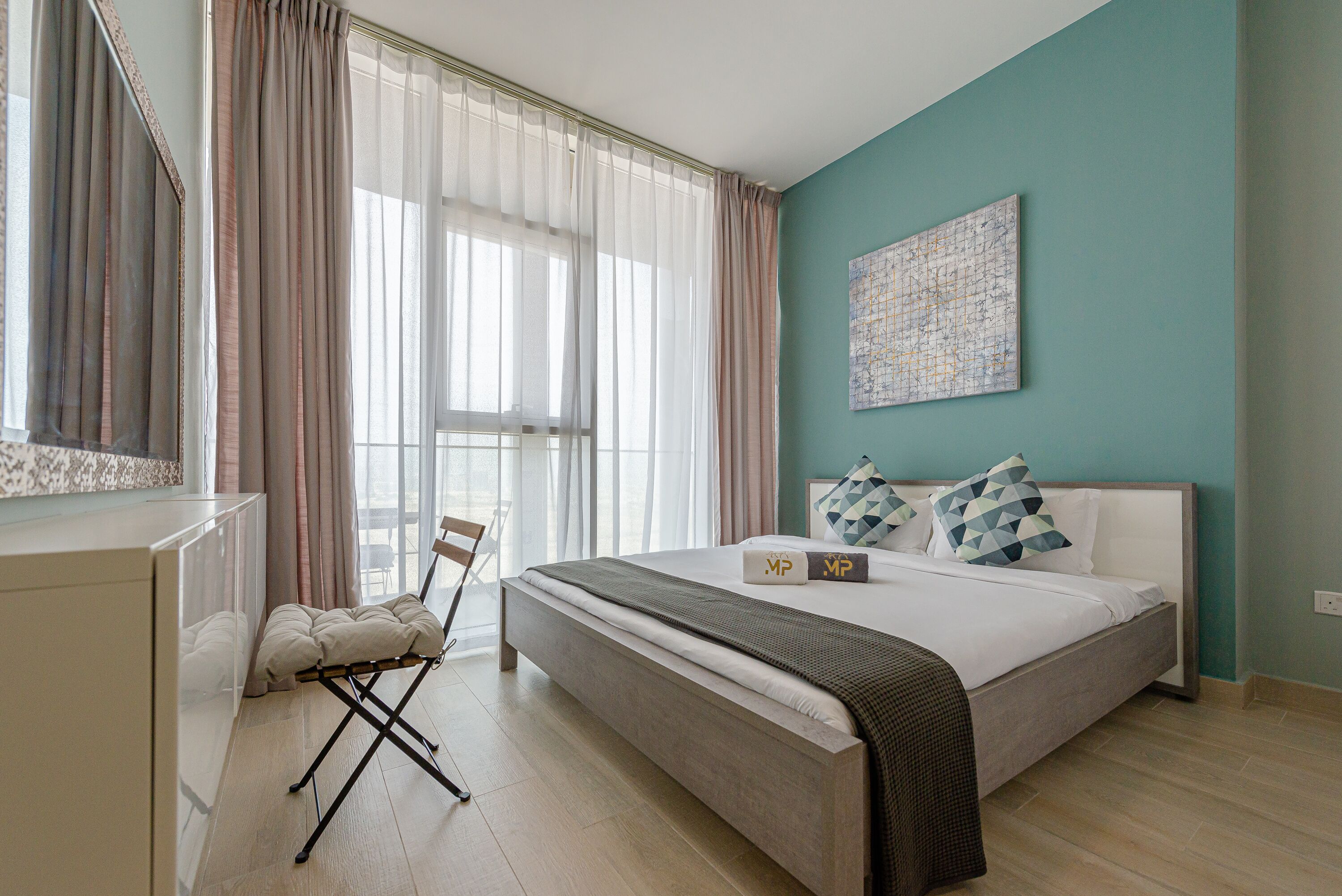 A bedroom with a bed, a chair, a desk, and a window with curtains.
