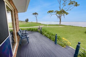 A wooden deck with outdoor seating, a view of a lake, and a grassy area with trees.
