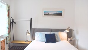 A neatly made bed with pillows and a blanket, a bedside table with a lamp, a radiator, and a picture on the wall. - City Centre Chichester Apartment, Peaceful Chichester Retreat, Sleeps 2 (Chichester)