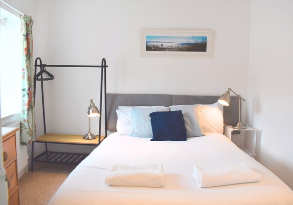 A neatly made bed with pillows and a blanket, a bedside table with a lamp, a radiator, and a picture on the wall.