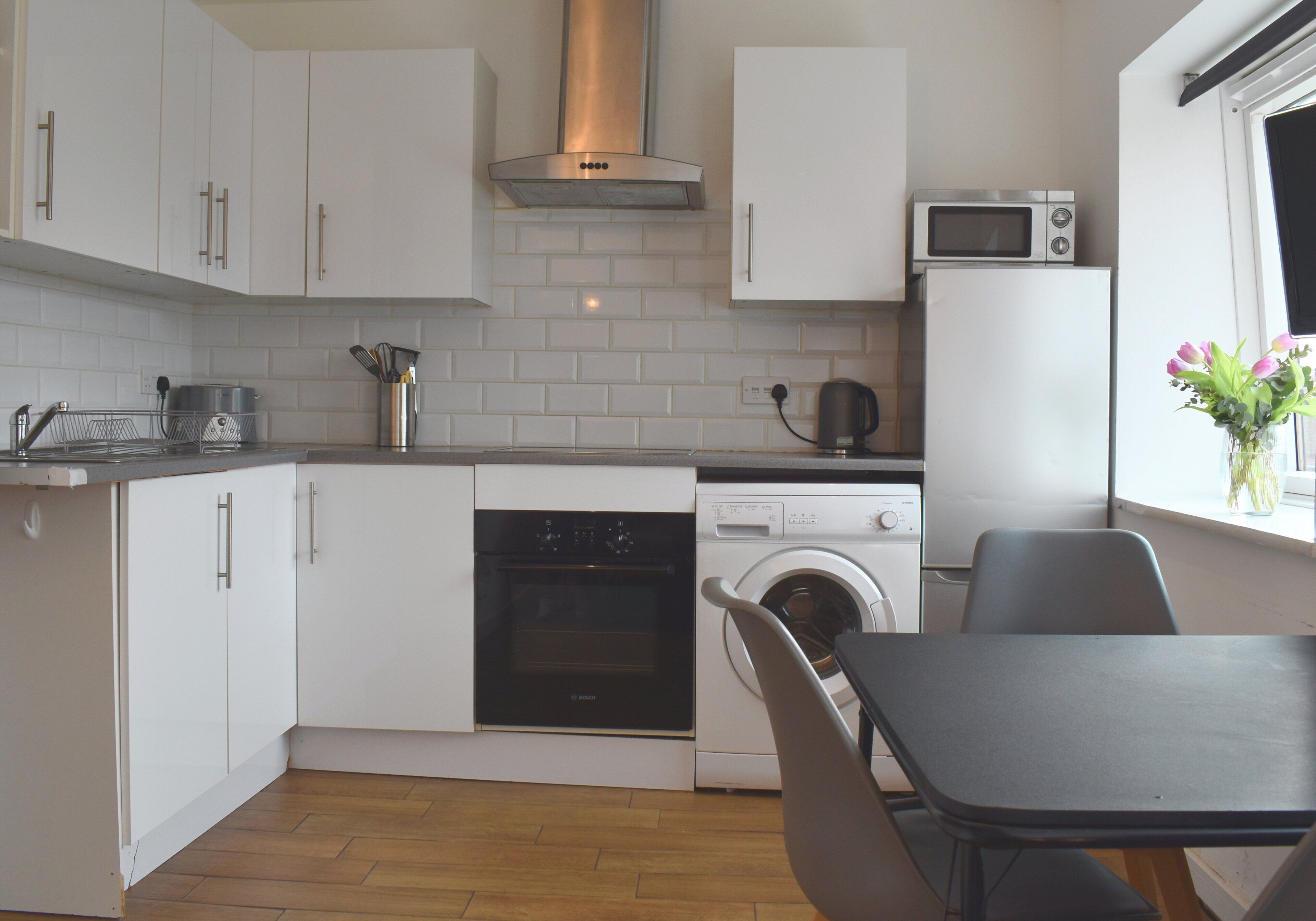 Une cuisine compacte avec des meubles blancs, un four à micro-ondes, un four traditionnel et un lave-linge.