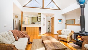 A spacious living area with a high ceiling, a fireplace, a kitchen with a view, and a cozy seating arrangement. - Malda's Retreat - Pet Friendly Absolute Beachfront (Culburra Beach)