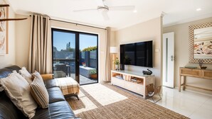 A modern living room with a sofa, TV, and a sliding glass door leading to a balcony. - Alkira - Pet Friendly - 4 Mins Walk to Beach (Culburra Beach)