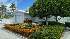 A residential house with a well-maintained garden, a large tree, and a white garage door.