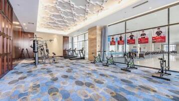 A hotel gym with exercise equipment, patterned carpet, and large windows.