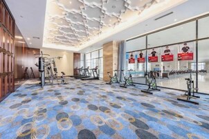 Un gimnasio de hotel con equipo de ejercicio, alfombra estampada y ventanas amplias.