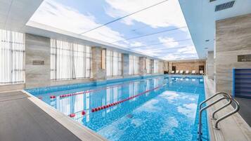 An indoor swimming pool with clear lanes, a diving board, and a view of the sky through the ceiling.
