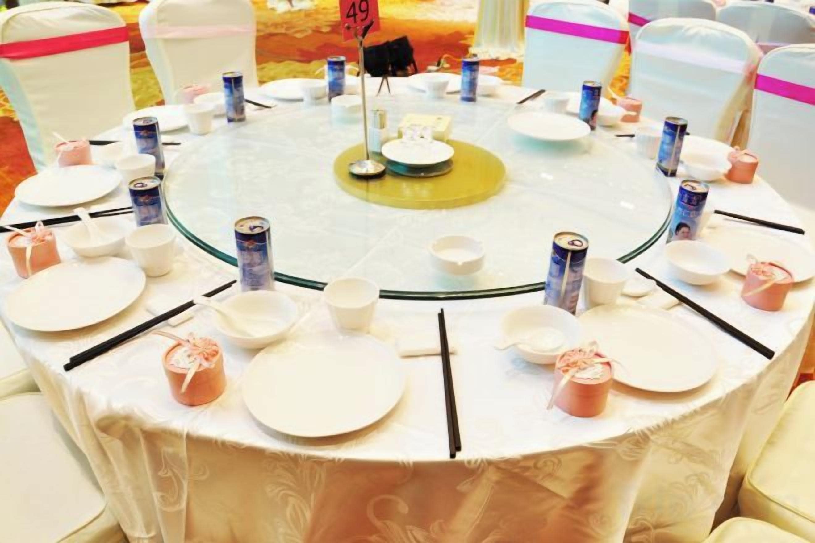 A round table with plates, cups, and cans, surrounded by chairs with pink sashes.