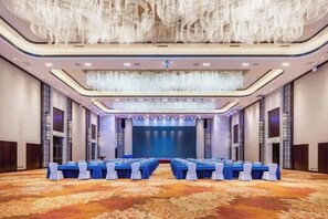 Un salón de conferencias con una larga mesa, sillas y un escenario al frente.