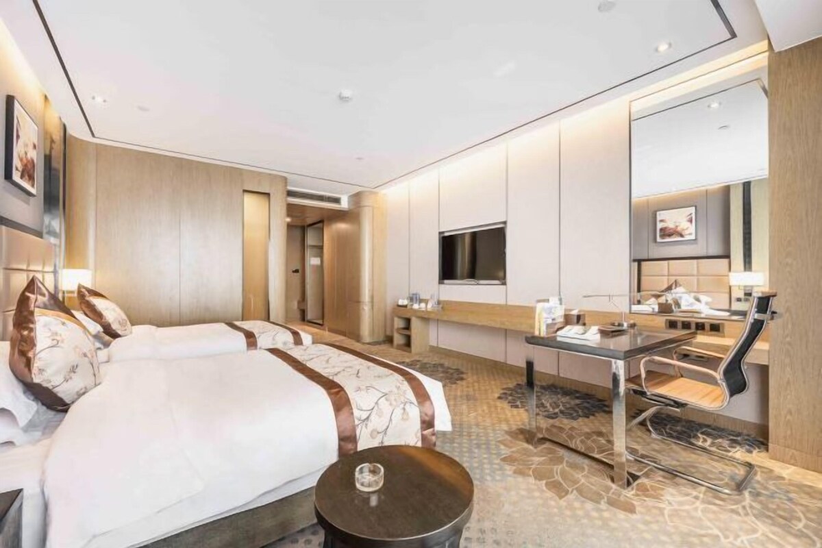 Een moderne hotelkamer met een groot bed, een bureau met stoel, een televisie en een spiegel.
