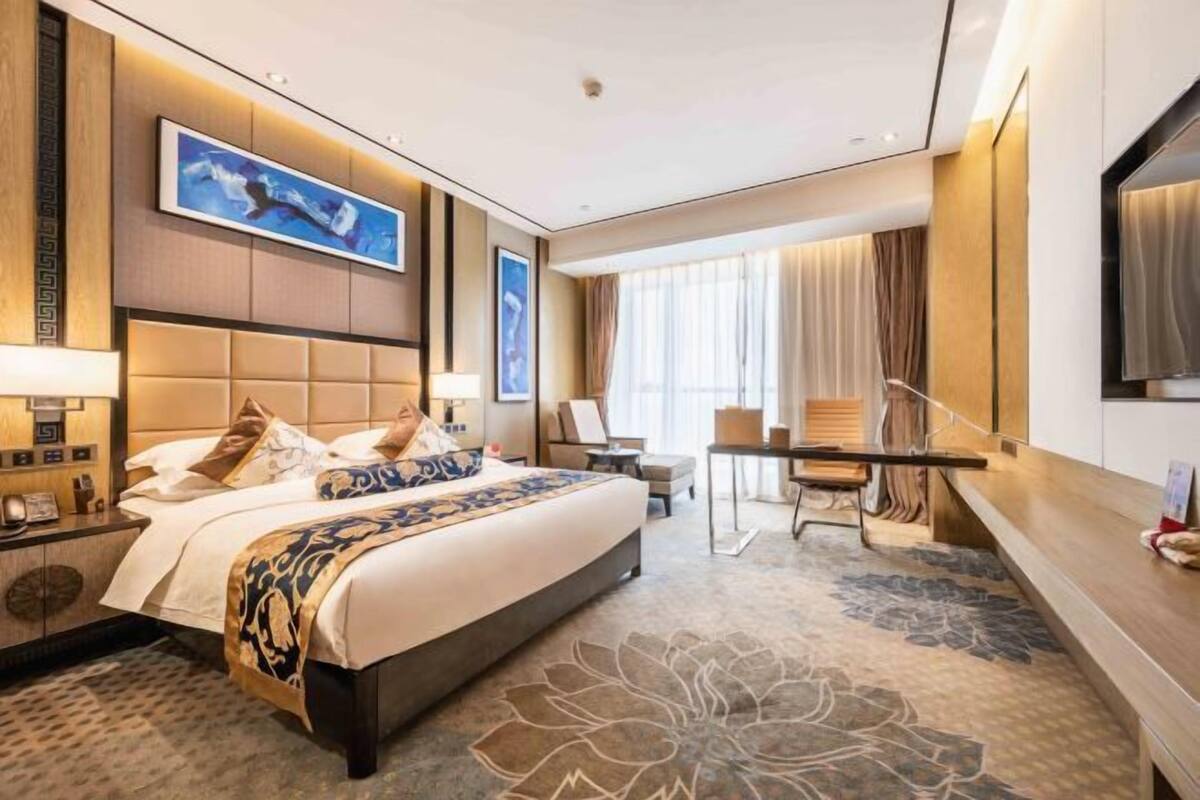 Ein Hotelzimmer mit einem großen Bett, einem Schreibtisch, einem Sessel und einem Fernseher.