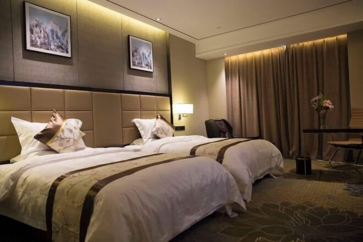 Ein Hotelzimmer mit zwei Betten, einem Schreibtisch, einem Sessel, einer Lampe und zwei gerahmten Bildern an der Wand.