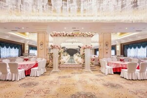 Un salón de banquetes con un pasillo central, sillas blancas y mesas dispuestas a ambos lados.
