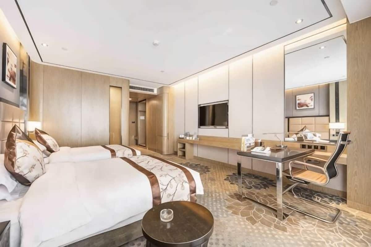 Ein Hotelzimmer mit zwei Betten, einem Schreibtisch, einem Fernseher und einem großen Spiegel.
