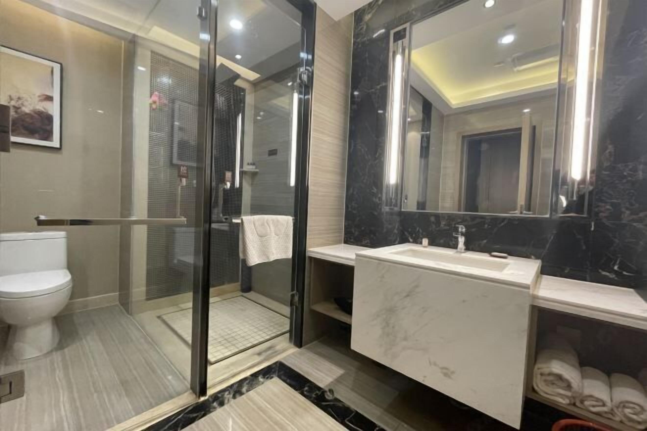 A modern bathroom with a glass-enclosed shower, a white toilet, a marble sink, and a large mirror.