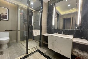 Een moderne badkamer met een douchecabine van glas, een wit toilet, een marmeren wastafel en een grote spiegel.