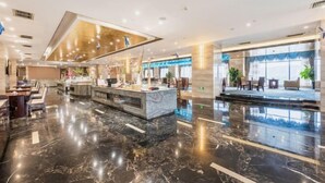 Un moderno vestíbulo de hotel con suelo de mármol, mostrador de recepción, zona de estar y escenario para eventos.