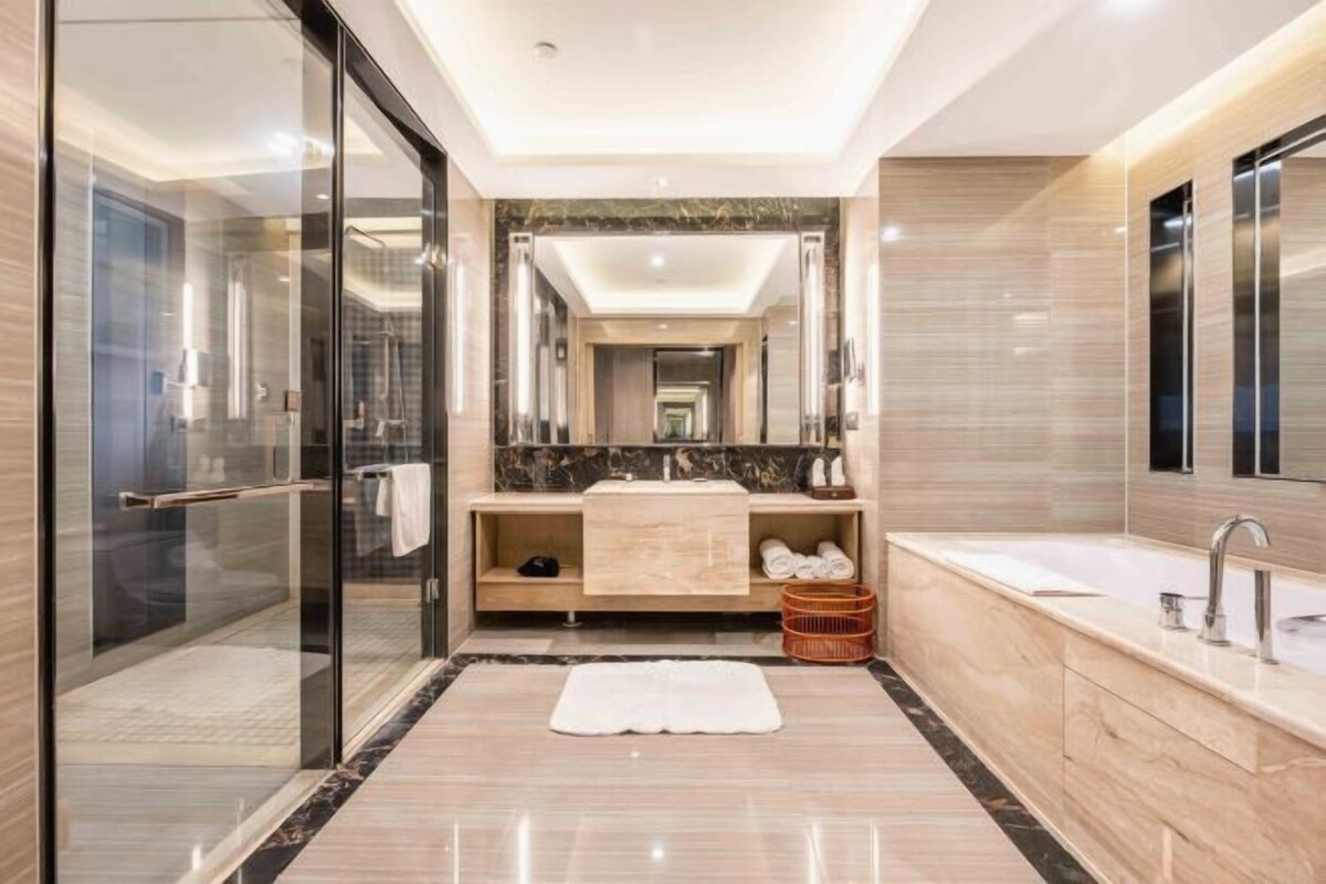 Een moderne badkamer met een glazen douchecabine, een marmeren wastafel en een grote spiegel.