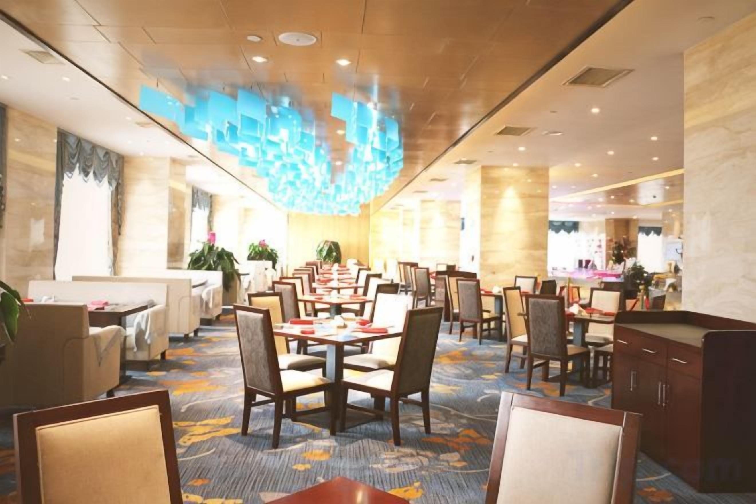 Comedor de hotel con varias mesas y sillas, alfombra estampada y un diseño moderno de techo.