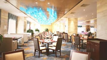Comedor de hotel con varias mesas y sillas, alfombra estampada y un diseño moderno de techo.