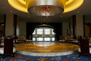 A lobby with a circular seating area, a large chandelier, and a view through a glass wall.