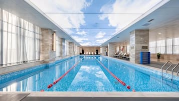 Una piscina interior con carriles delimitados, suelo de baldosas y vista al cielo a través del techo.