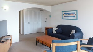 A living room with a dark blue sofa, a wooden coffee table, and a TV stand. There is a framed picture on the wall and a door leading to a closet. - Lakeside. Breezy. Serendipity. (Forster)