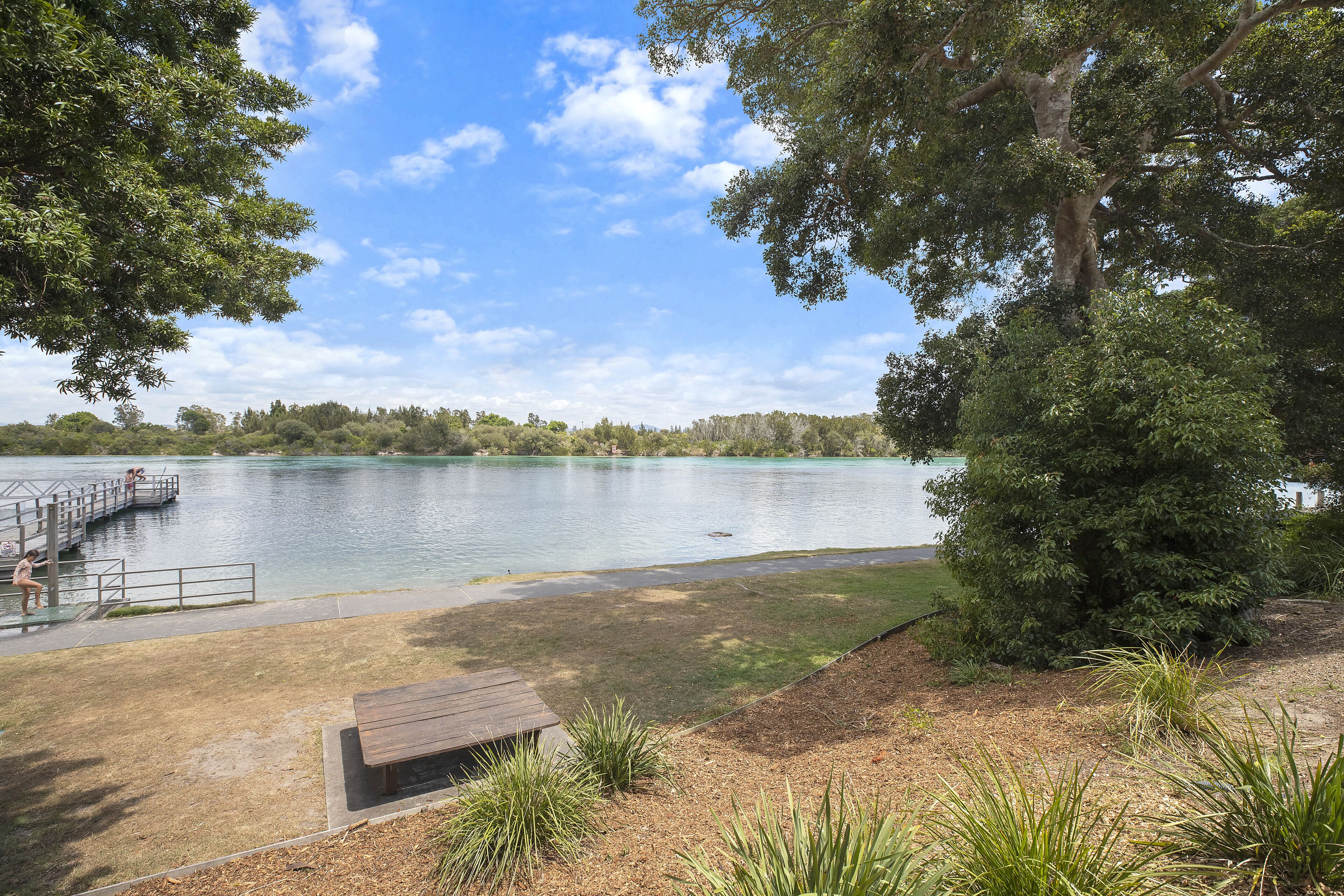Un parc au bord du lac, avec un banc en bois, une jetée et une zone herbeuse.