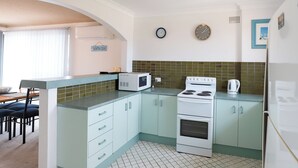 A compact kitchen with a microwave, stove, and refrigerator. There is a dining table with chairs and a window with blinds. - Lakeside. Breezy. Serendipity. (Forster)