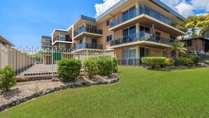 A modern multi-story residential building with balconies, a well-maintained lawn, and a gated entrance. - Lakeside. Breezy. Serendipity. (Forster)