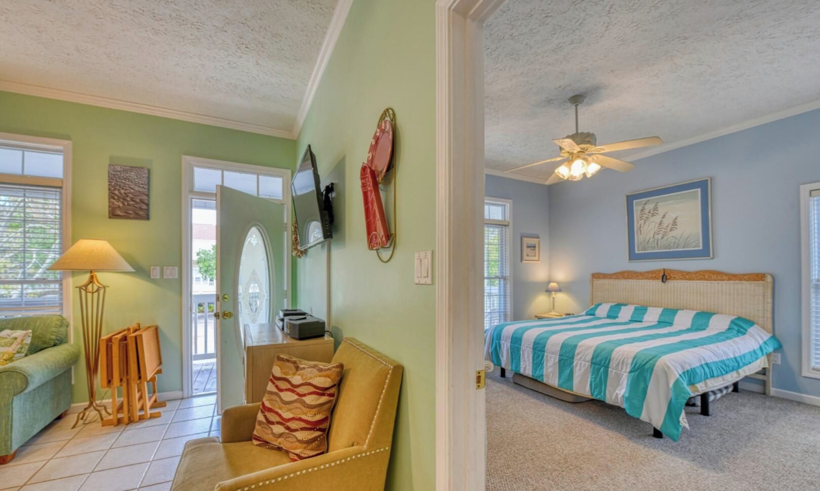 A room with a bed, a chair, a lamp, a ceiling fan, and a door leading to another room.