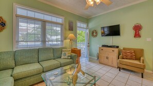 A living room with a green sofa, a glass coffee table, a wooden cabinet, and a television on the wall. - Piper's Retreat - Four Bedroom, Three Bath Dog Friendly Home (Surfside Beach)