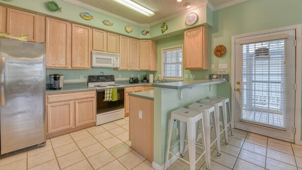 A kitchen with wooden cabinets, a stainless steel refrigerator, a microwave, and a stove. There are stools near the counter and a window with blinds. - Piper's Retreat - Four Bedroom, Three Bath Dog Friendly Home (Surfside Beach)