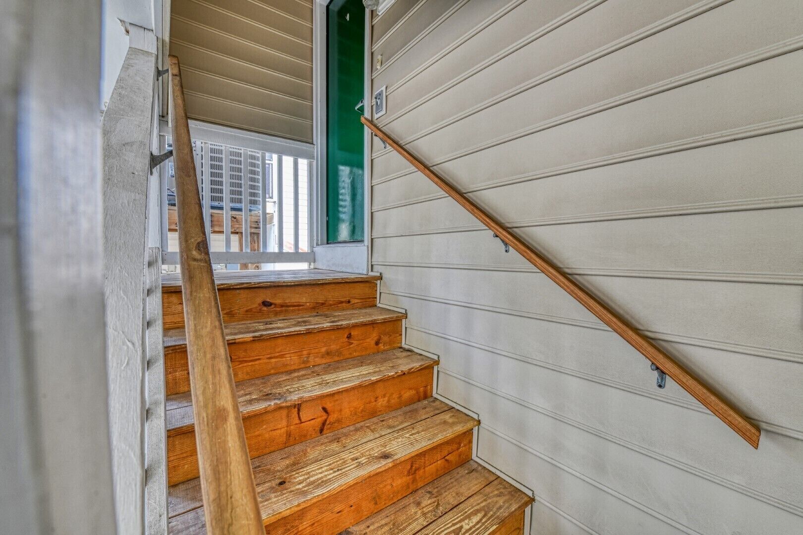 A wooden staircase with a handrail leading to a green door.